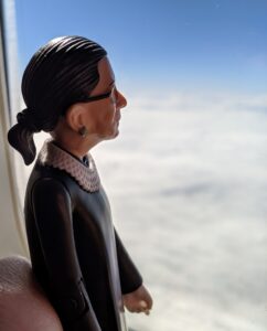 A figurine of Ruth Bader Ginsburg looks out an airplane window