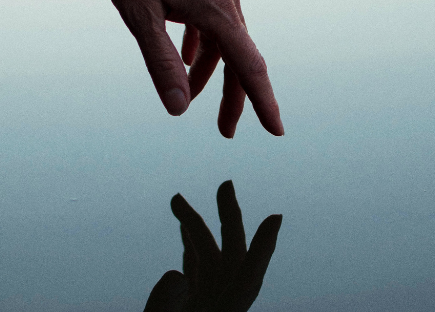 a hand reaches toward the water and is reflected