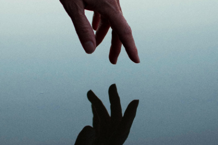 a hand reaches toward the water and is reflected