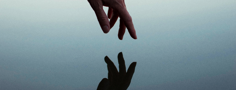 a hand reaches toward the water and is reflected