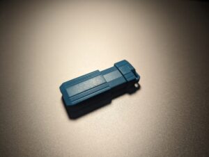 In an oversaturated photo, a bright blue jump drive sits on a silver laptop case.