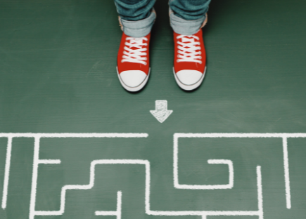 Two feet, clad in red Chucks, stand at the entrance of a maze on a green floor.