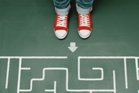 Two feet, clad in red Chucks, stand at the entrance of a maze on a green floor.