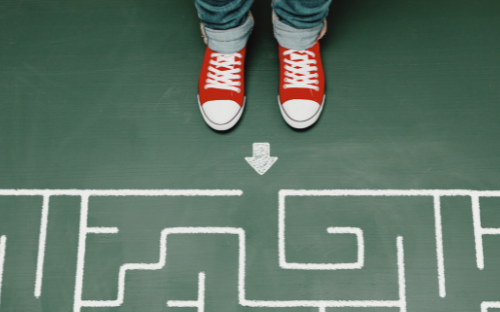 Two feet, clad in red Chucks, stand at the entrance of a maze on a green floor.