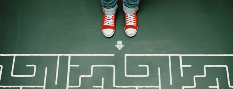 Two feet, clad in red Chucks, stand at the entrance of a maze on a green floor.