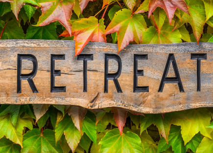 A wooden sign reading "retreat" with green foliage in the background